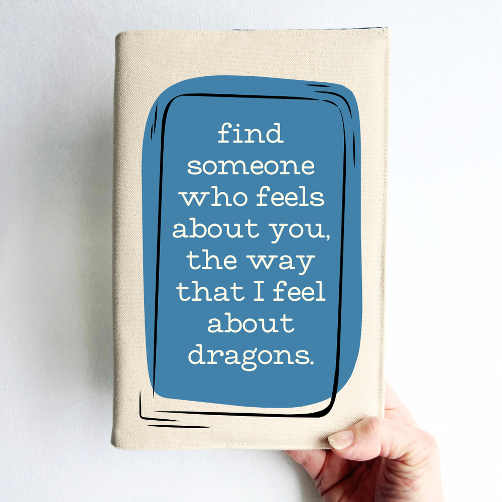 a hand holding a book covered in linen-color reusable canvas adjustable book cover. A blue square is the background for the words, 'find someone who feels about you, the way that I feel about dragons.' in white lettering.