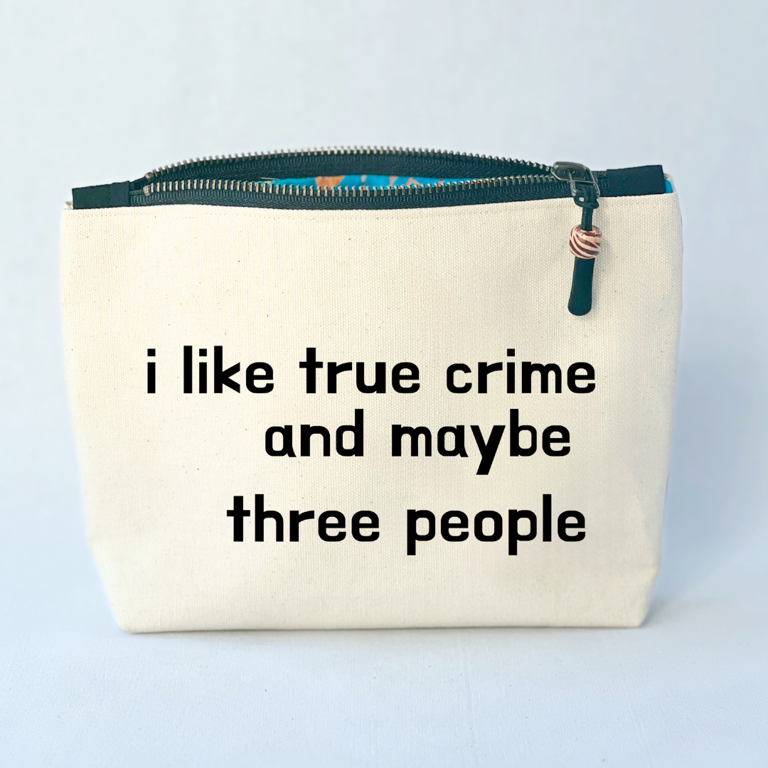 A linen-color square canvas zip bag with a black zipper and the words, I like true crime and maybe three people
