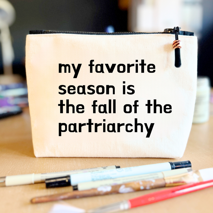 square linen-color canvas zip bag with black zipper and the words, my favorite season is the fall of the patriarchy.