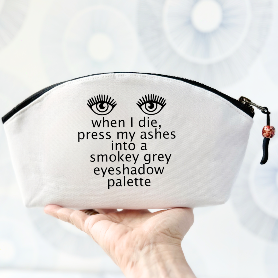 white canvas bag with curved top and black zipper, with the words, when I die, press my ashes into a smokey grey eyeshadow palette
