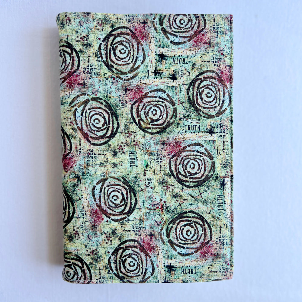 a book covered in a vibrant blue green fabric reusable  adjustable book cover.  Fabric has impressionist rose / concentric deep brown circles and the word ' TRUTH scattered on the pattern.