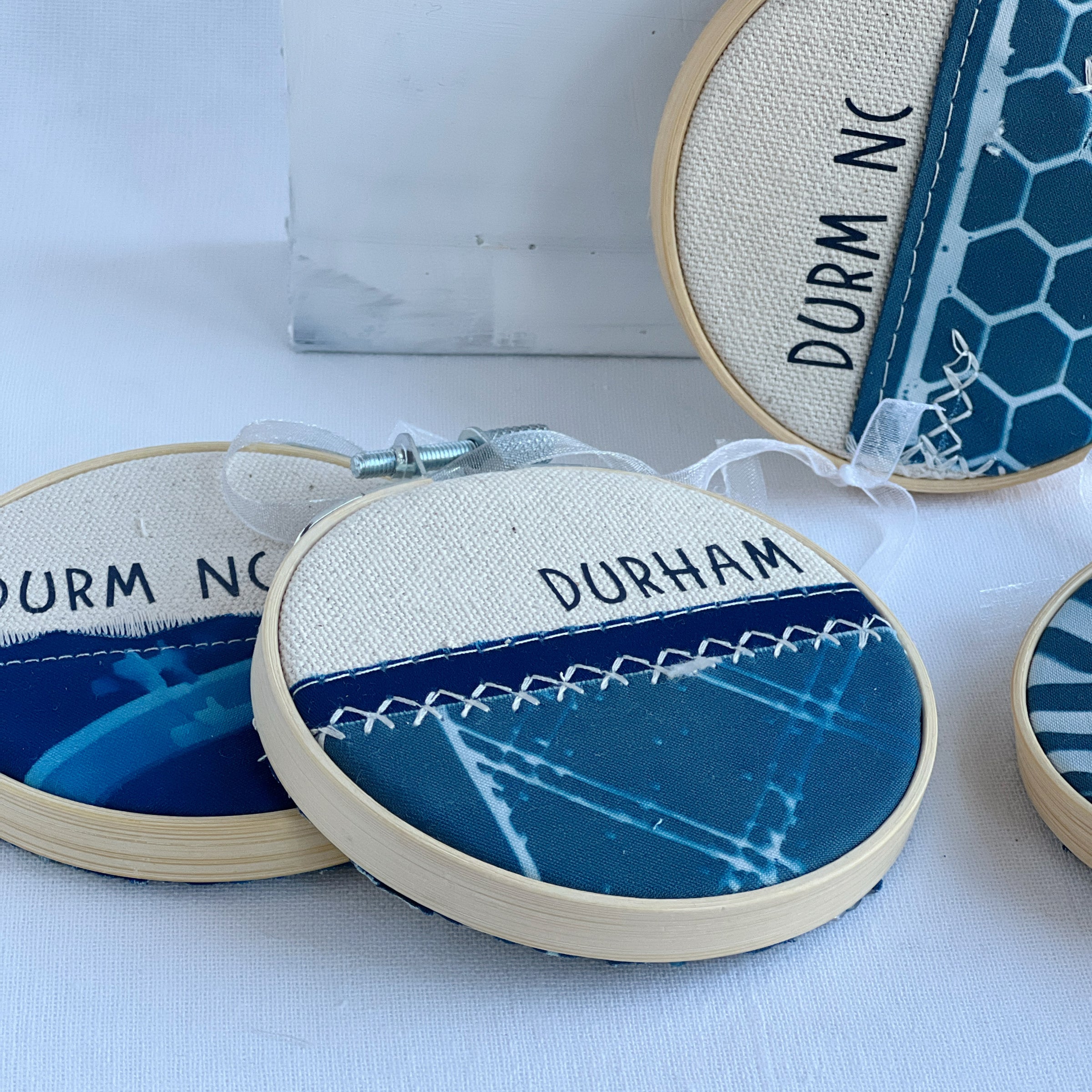 dyed wooden embroidery hoop with painted fabric in yellows, oranges and greens. Stitching to form an old bridge. In black vinyl, a quote on the front says, "for her the ocean was more than a dream. it was a place she needed to visit to find herself.