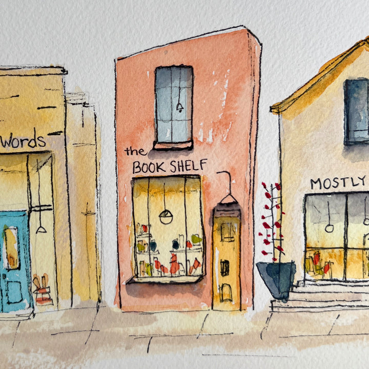A watercolor art print depicting four stone bookstore buildings, presented with a wide white mat board against a neutral gray background.
