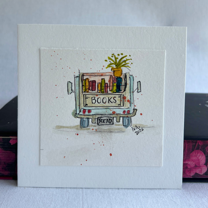 A square watercolor original art print featuring a hand-drawn and hand-painted illustration of a book cart with the word 'BOOKS' on the back and a small plant on top, displayed upright on stacked books.