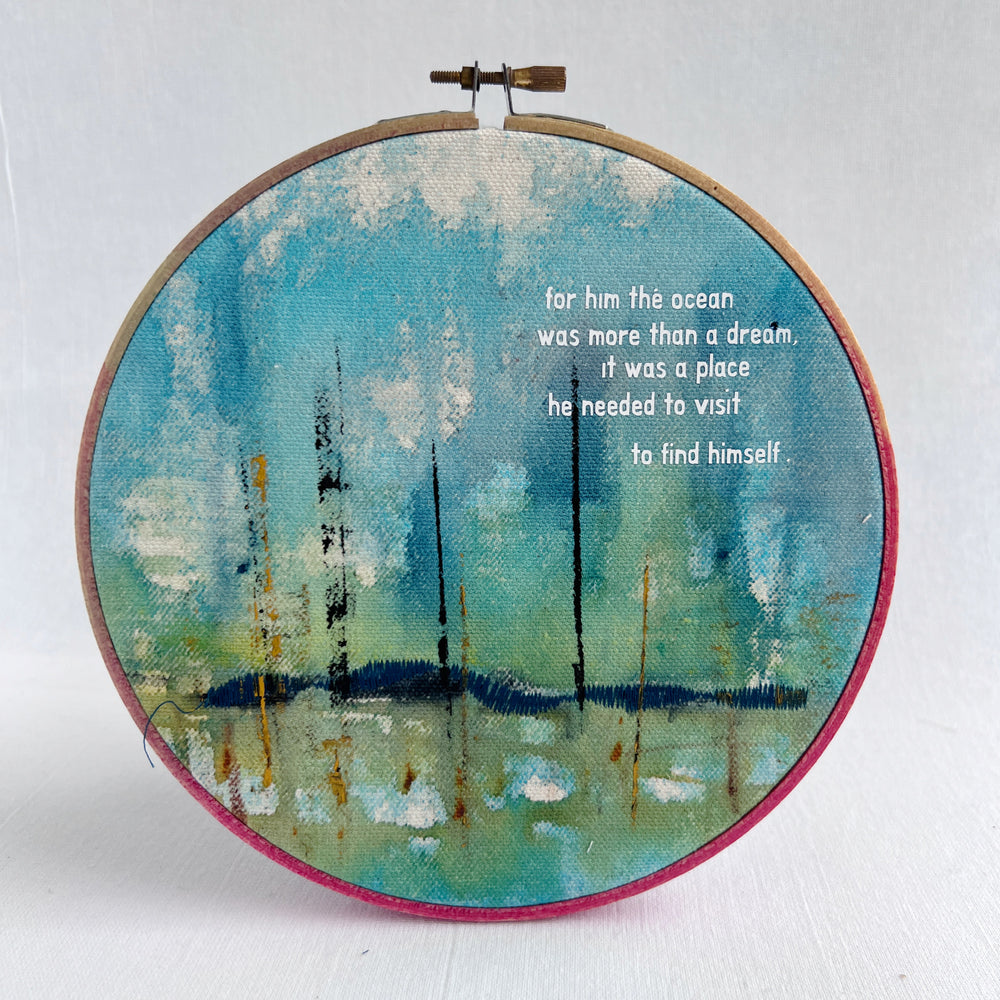 A large painted hoop art piece, with bright blues, citron green and touches of white. stitched with a deep blue shoreline and finished with the words, for him, the ocean was more than a dream. it was a place he needed to visit to find himself. 