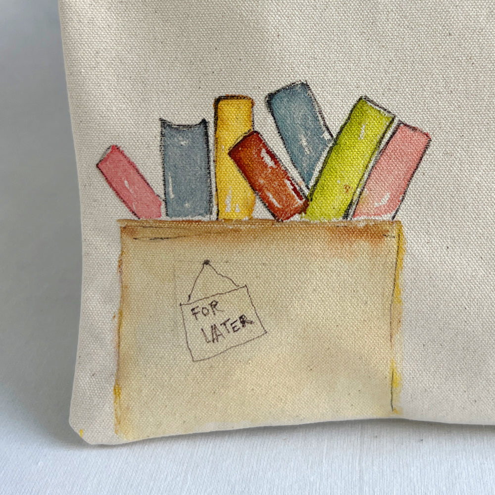 A close-up of a beige canvas or linen fabric item, likely a small pouch or bag, featuring a hand-painted illustration of colorful chalk sticks in a brown box with a handwritten tag that says 'FOR LATER'.