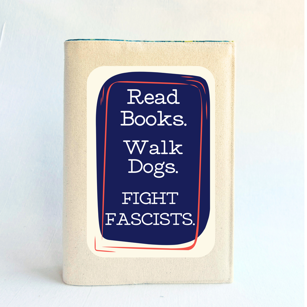 A canvas, reusable book cover in linen, with the words, 'Read Books. Walk Dogs. FIGHT FASCISTS.'  in white lettering placed on a rectangular navy box design.