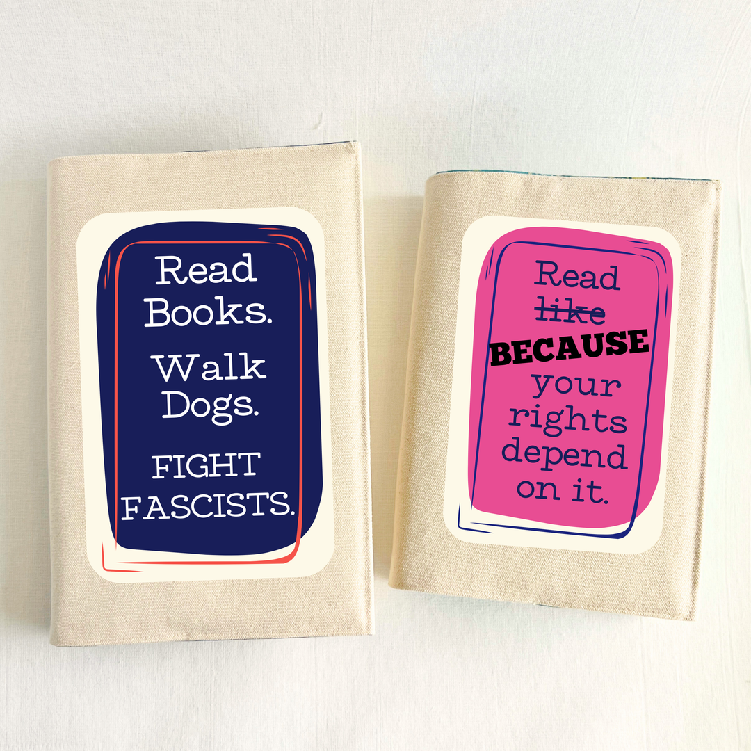Canvas, reusable book covers in linen, with the words, 'Read Books. Walk Dogs. FIGHT FASCISTS.'  in white lettering placed on a rectangular navy box design on one cover, and 'Read like (because) your rights depend on it' in navy lettering on a pink box design.