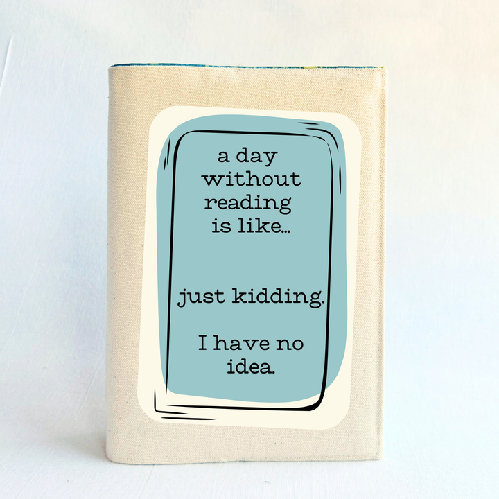 A canvas, reusable book cover in linen, with the words, 'a day without reading is like.. just kidding. I have no idea. ' in black lettering, placed on a rectangular light blue box design.