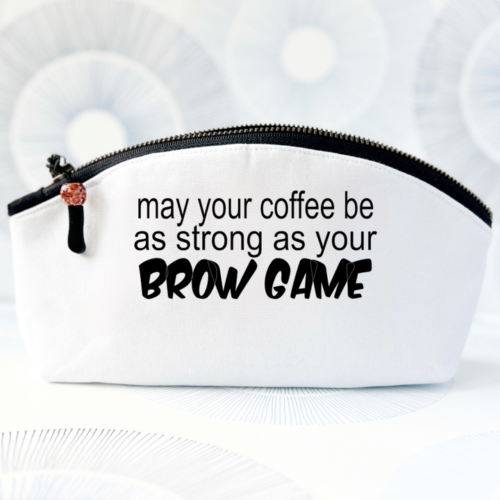 white canvas bag with a curvy top, a black zipper and the words, may your coffee be as strong as your brow game.