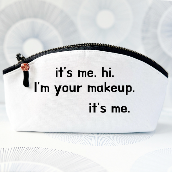 white canvas makeup bag with a curvy top, a black zipper and the words, it's me. hi. I'm your makeup. it's me.