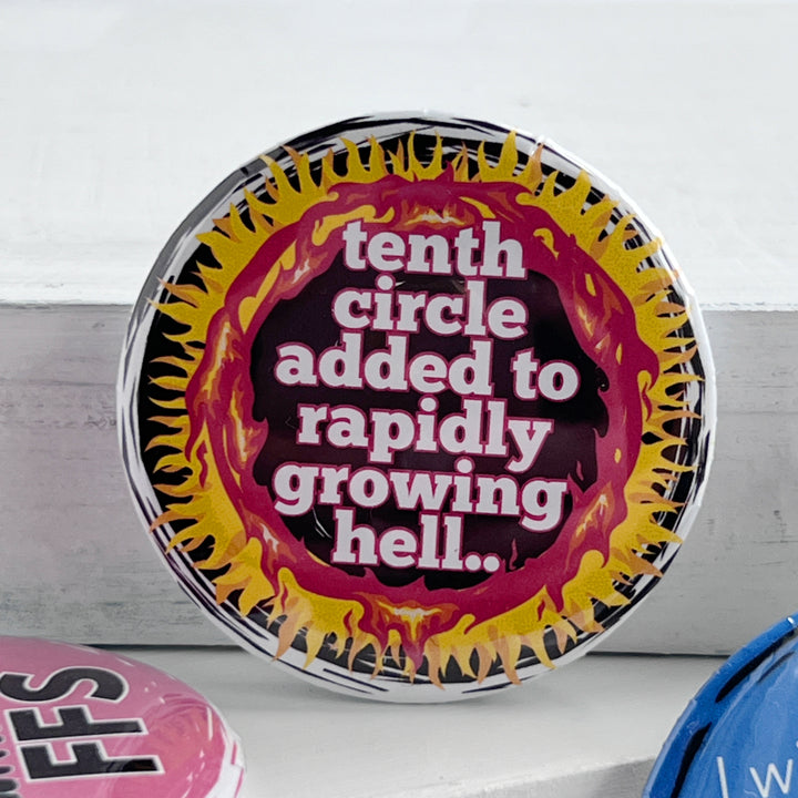 round pinback button with a black background, yellow and red flames surrounding the words, "tenth circle added to rapidly growing hell."