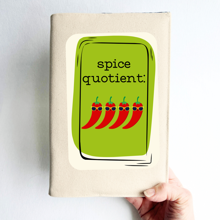 a book covered in linen-color reusable canvas adjustable book cover. A bright green square is the background for the words, 'spice quotient' in black lettering. Four cartoon peppers with sunglasses are layered on top.