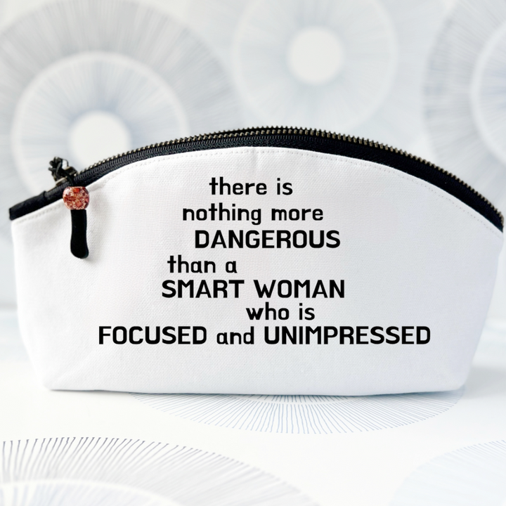 white canvas bag with curvy top, black zipper and the words, there is nothing more dangerous than a smart woman who is focused and unimpressed