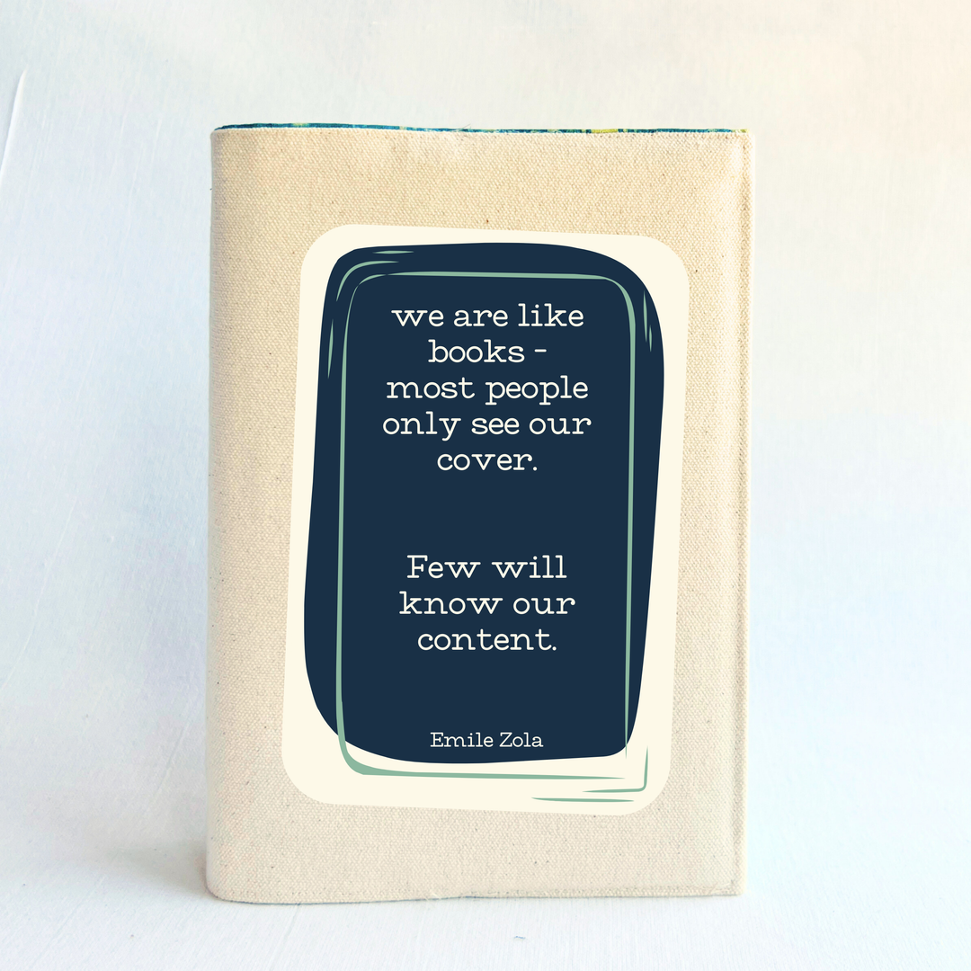 a book covered with a linen-colored canvas reusable book cover.  A rectangular design in navy tops the cover, with the words, 'we are like books - most people only see our cover.  Few will know our content.' a quote by Emile Zola, done in white lettering.