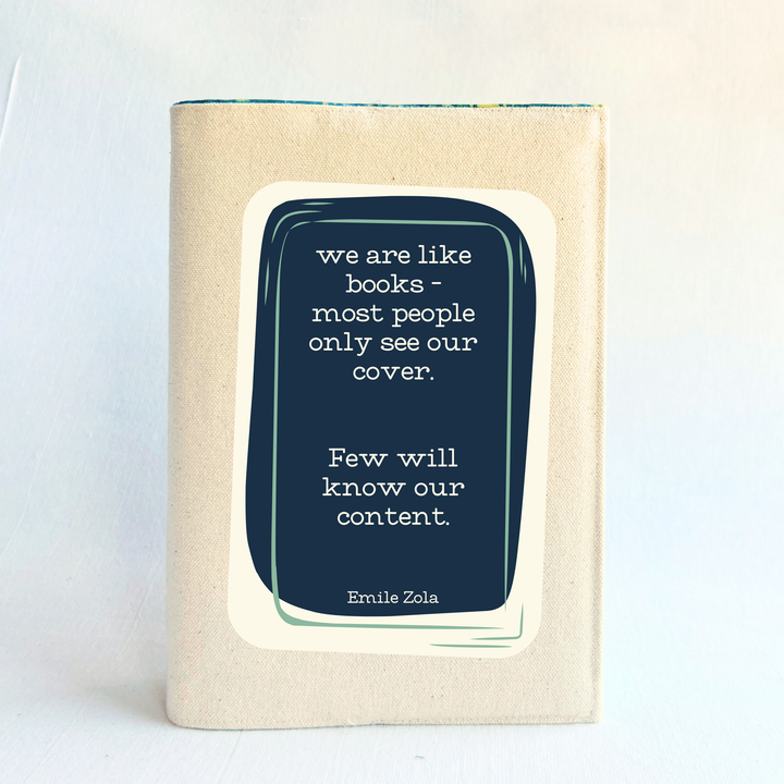 a book covered with a linen-colored canvas reusable book cover.  A rectangular design in navy tops the cover, with the words, 'we are like books - most people only see our cover.  Few will know our content.' a quote by Emile Zola, done in white lettering.