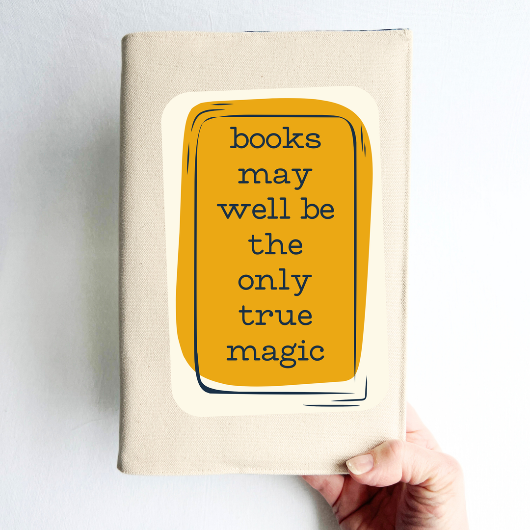 a hand holding a book covering in linen-colored canvas fabric, with the words, 'books may well be the only true magic' in black lettering on a deep orange yellow box design.