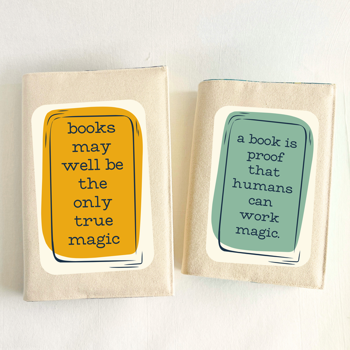 a hand holding a book covered with a linen-colored canvas reusable book cover. A rectangular design in sage green is featured in the center of the cover, with the words, 'a book is proof that humans can work magic.' A second book cover in yellow-orange has the words, 'books may well be the only true magic.'