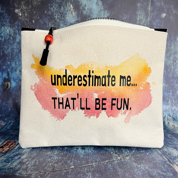 a canvas zip bag with watercolor paints and the words, "underestimate me, that'll be fun" in black lettering