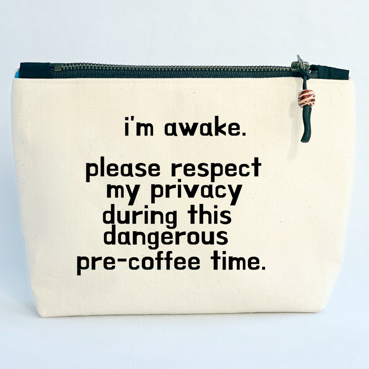 square linen-color canvas zip bag with a black zipper and the words, I'm awake. please respect my privacy during this dangerous pre-coffee time.