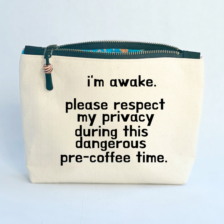 square linen-color canvas zip bag with a black zipper and the words, I'm awake. please respect my privacy during this dangerous pre-coffee time.