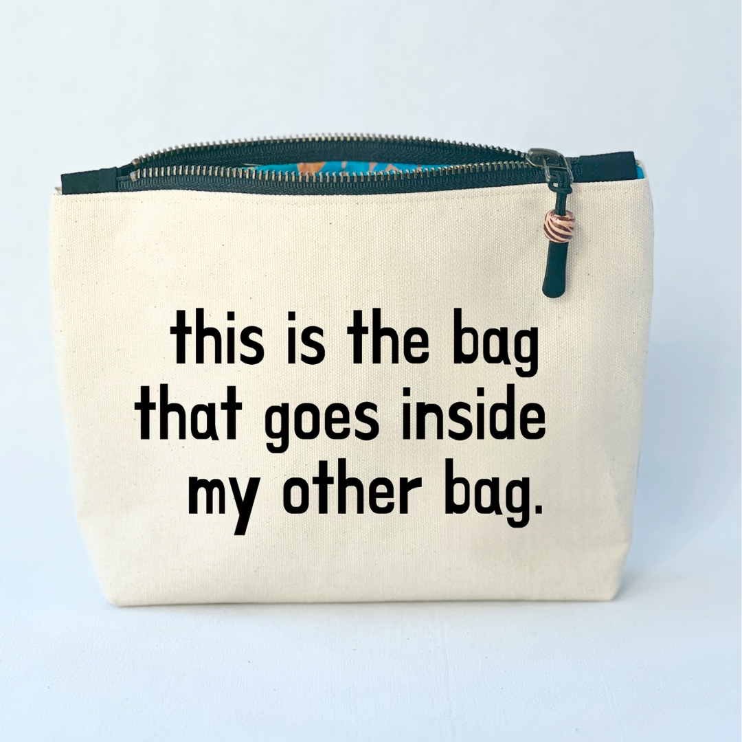 square linen-color canvas zip bag with black zipper and the words, this is the bag that goes inside my other bag.