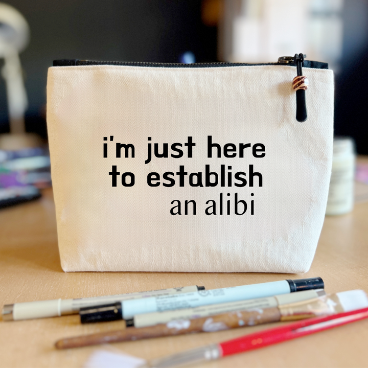 square canvas zip bag with black zipper and the words, I'm just here to establish an alibi