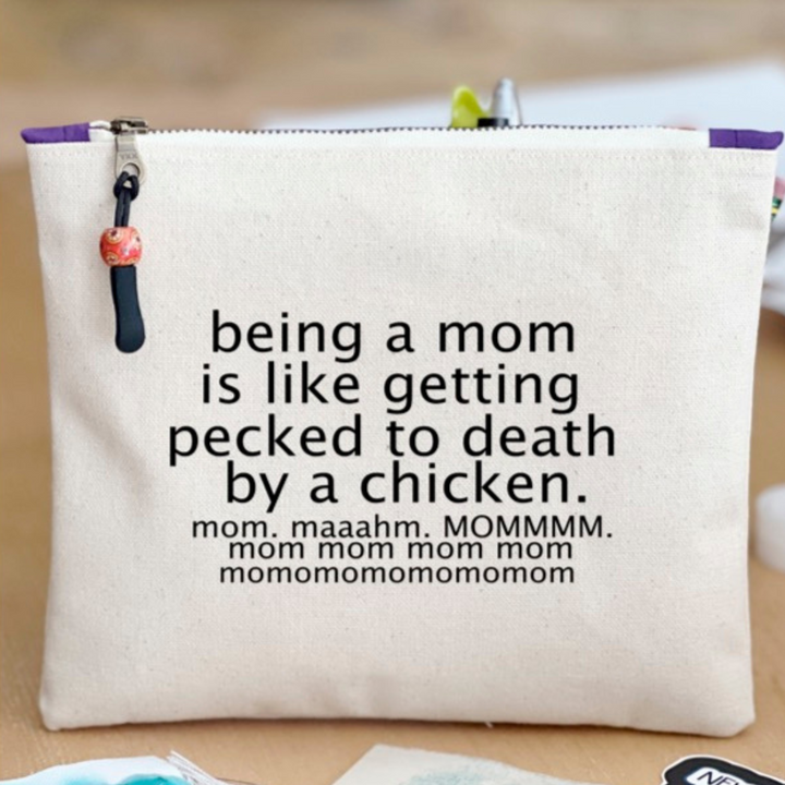 canvas zip bag measuring 9x7 with the words, "being a mom is like getting pecked to death by a chicken. mom. maahm. MOMMMMM!" in black lettering.