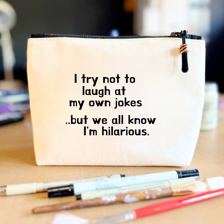 square linen-color canvas zip bag with a black zipper and the words, I try not to laugh at my own jokes..but we all know I'm hilarious
