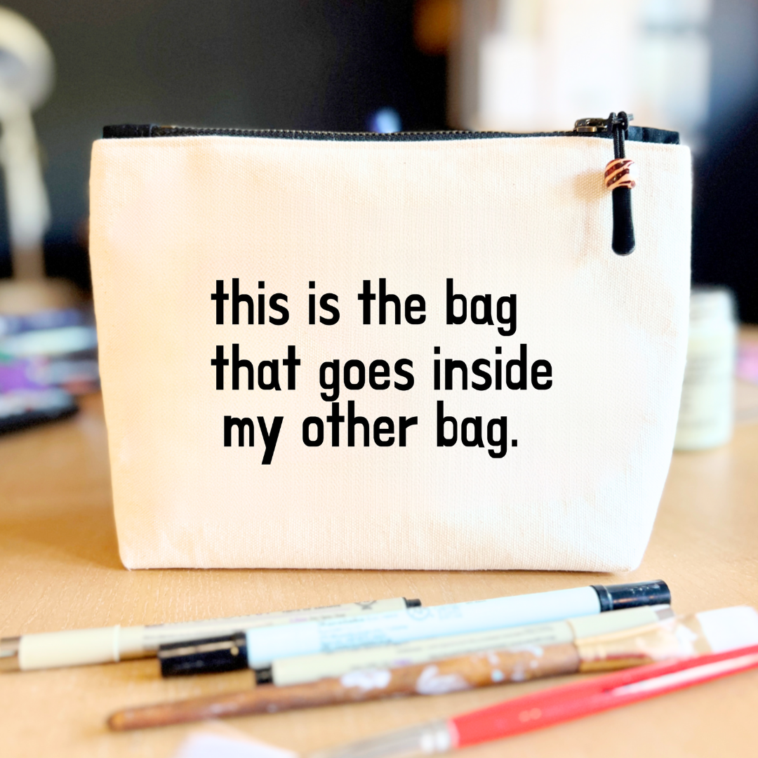 square linen-color canvas zip bag with black zipper and the words, this is the bag that goes inside my other bag.
