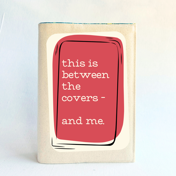 a linen-colored canvas book cover with a rose and cream graphic cover that reads 'this is between the covers - and me.' against a plain light background.