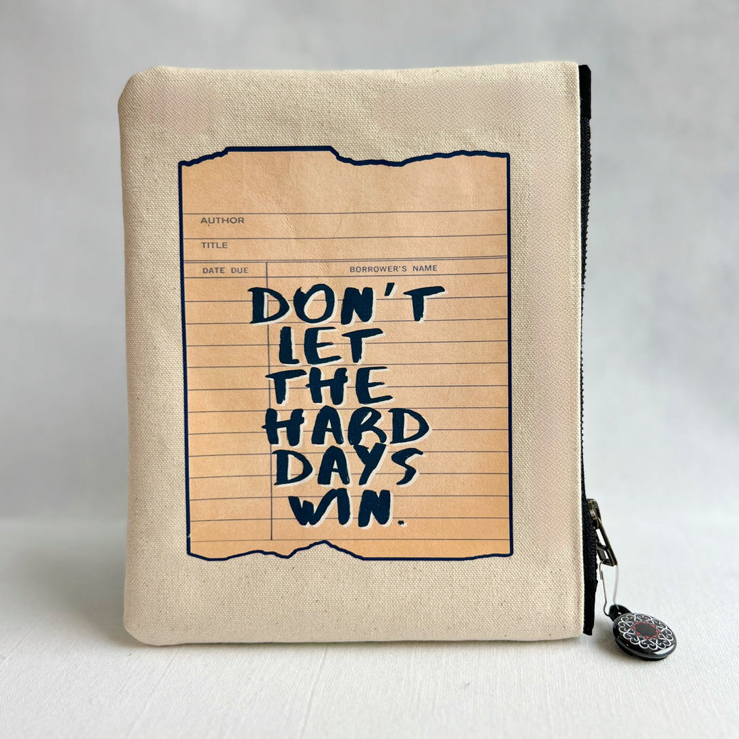 padded canvas zip bag with a green library card and the words, Don't Let the Hard Days Win, plus a colorful zipper pull and lining