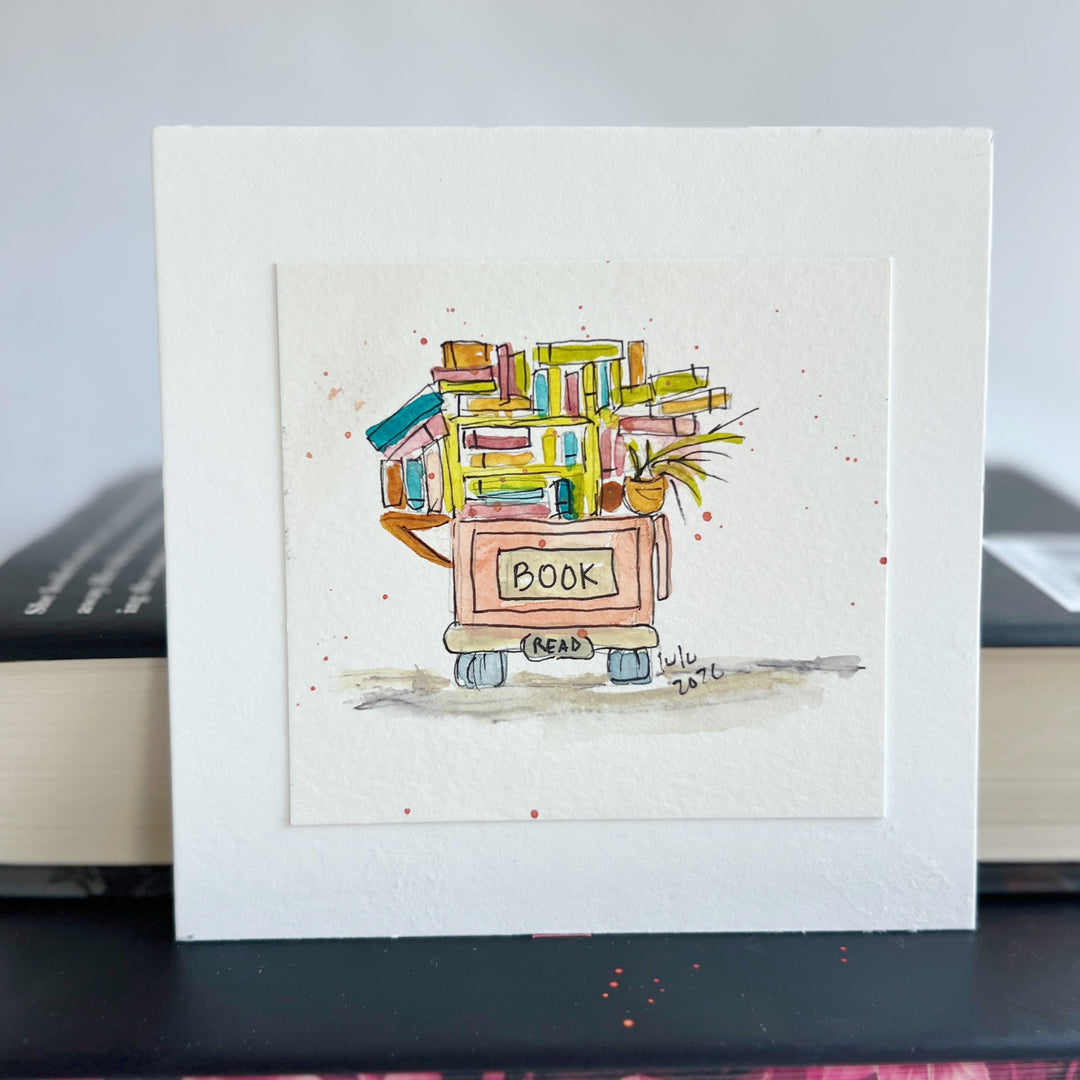 A square watercolor art print depicting a small book cart overfilled with colorful books and a potted plant, with the word “BOOK” written on the front.