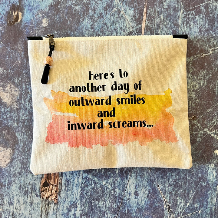 square canvas zip pouch with the words, Here's to another day of outward smiles and inward screams.'