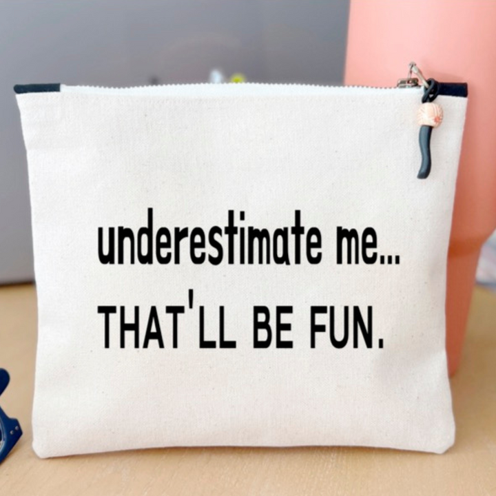 a canvas zip bag with the words, "underestimate me, that'll be fun" in black lettering