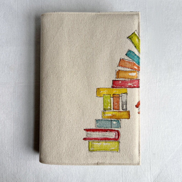 A canvas linen book cover featuring a hand-painted stack of colorful books on the right side.