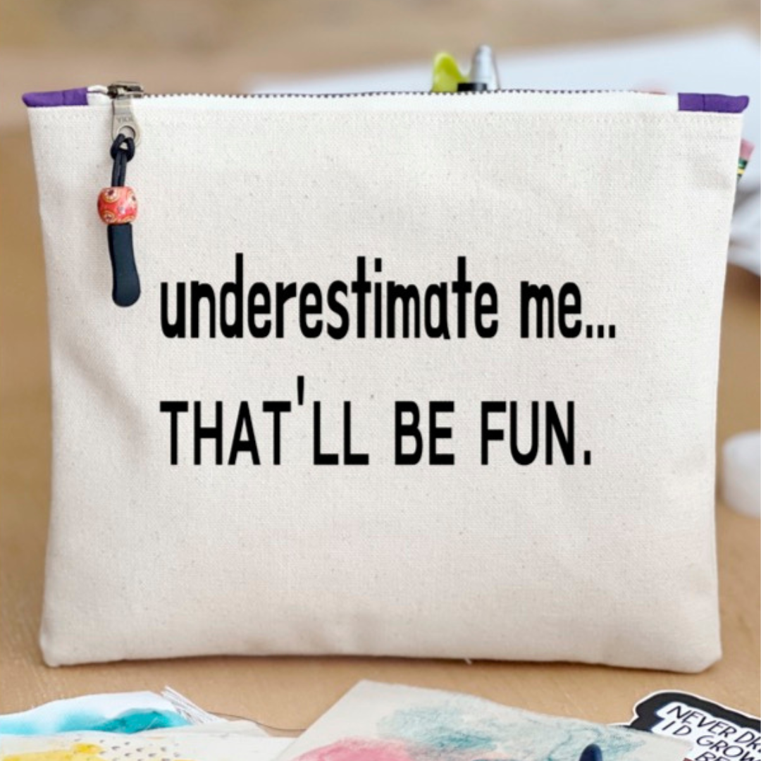 a canvas zip bag with the words, "underestimate me, that'll be fun" in black lettering