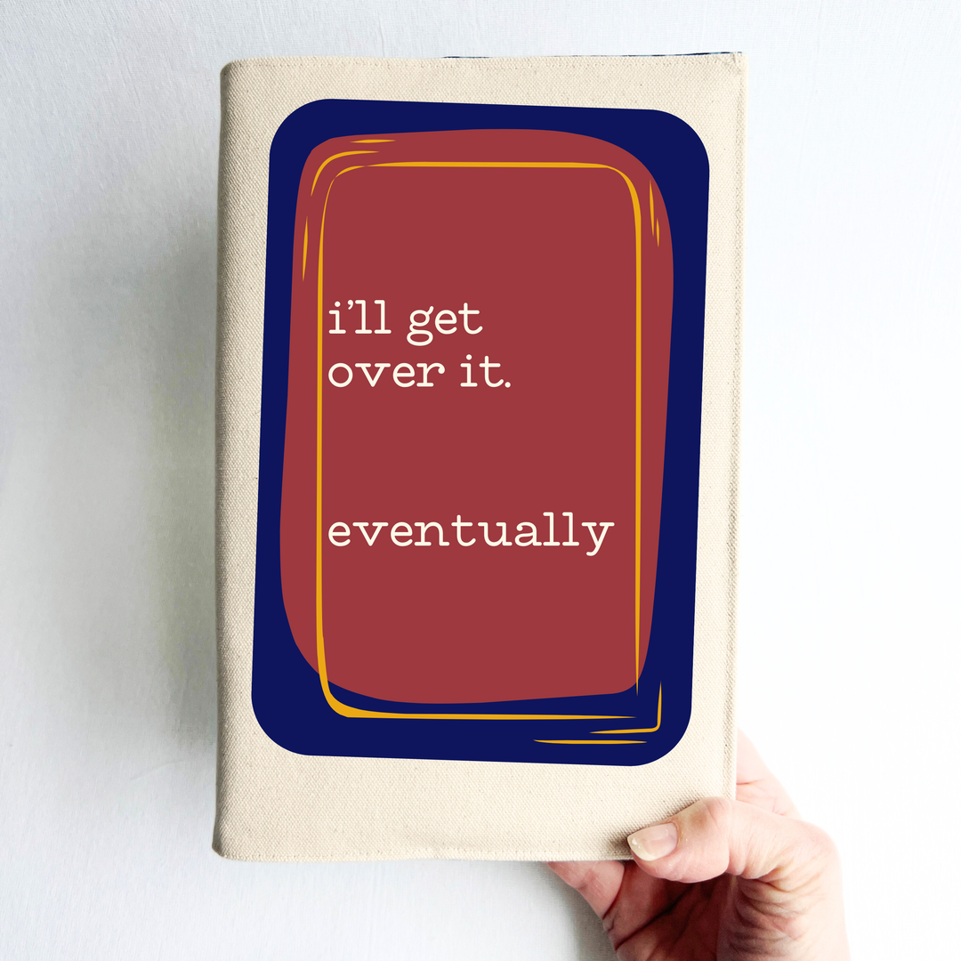 A hand holding a linen-colored canvas book cover with a graphic cover design. The design features a dark navy blue rounded rectangle with a red-orange center, outlined in yellow, containing the white text 'i'll get over it.'