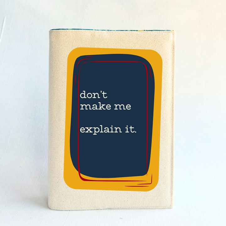 A linen-colored canvas book cover with a central graphic featuring a dark navy blue rectangle with white text that reads 'don't make me explain it.' The graphic is framed by a mustard yellow shape with thin red and orange accents