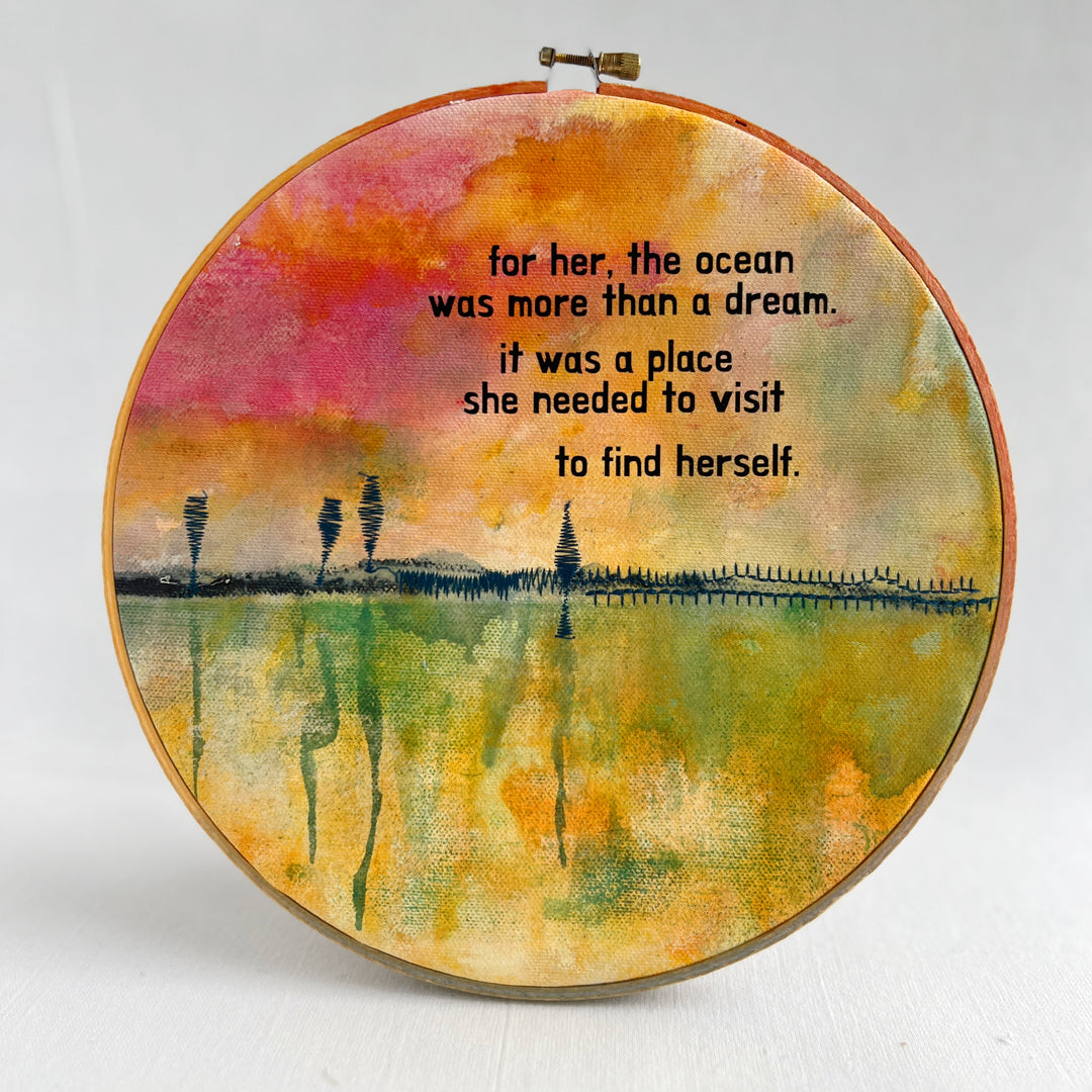 A large painted hoop art piece, with rose pinks, fresh greens and vibrant yellows, stitched with a rickety pier and finished with the words, for here, the ocean was more than a dream. it was a place she needed to visit to find herself. 