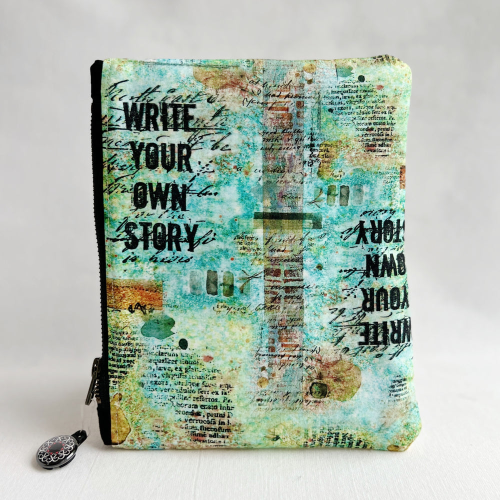 padded canvas zip bag with a mix of green and blue fabric and the words, Write Your Own Story, plus a colorful zipper pull and lining