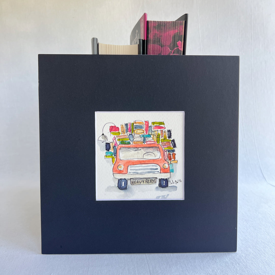 A square original watercolor art print depicting a red pickup truck loaded with colorful books and a wonky reading light, with the license plate reading 'HEAVY READS' 