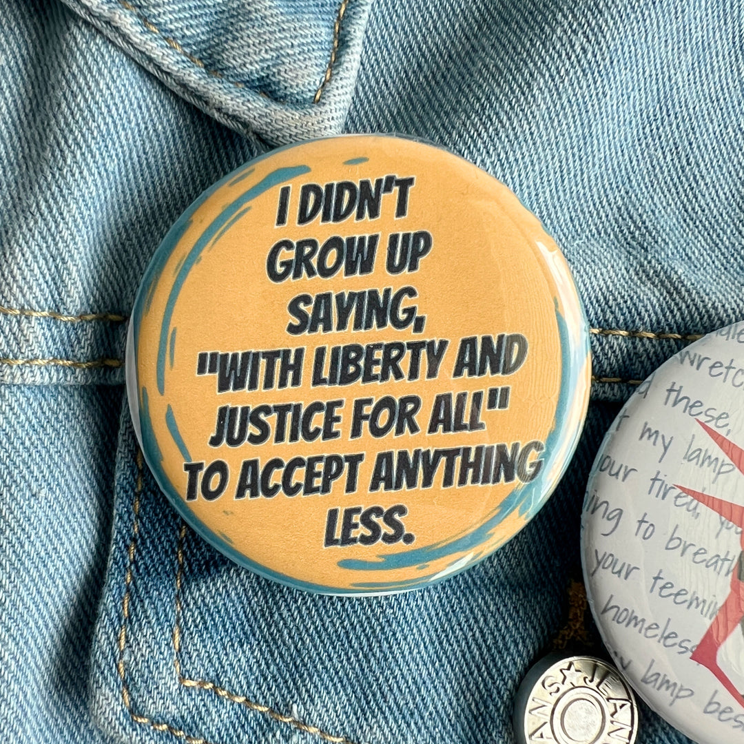 round pinback button with black lettering on a yellow background and the words, 'I didn't grow up saying "with liberty and justice for all" to accept anything less.' Pinned to a jean jacket for display