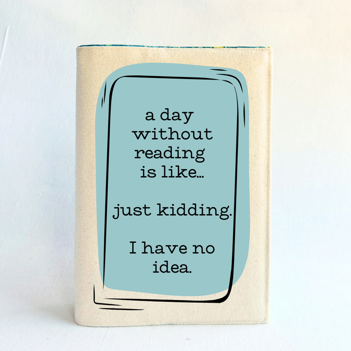 A canvas, reusable book cover in linen, with the words, 'a day without reading is like.. just kidding. I have no idea. ' in black lettering, placed on a rectangular light blue box design.