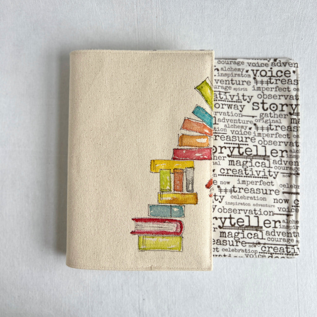 A canvas linen book cover featuring a hand-painted stack of colorful books with words on fabric for the inside of the cover