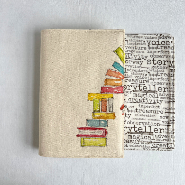 A canvas linen book cover featuring a hand-painted stack of colorful books with words on fabric for the inside of the cover
