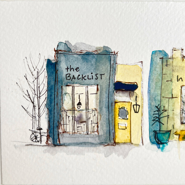 A horizontal watercolor art print depicting four whimsical bookstores with names including 'The Backlist', 'In the Margin, 'Paper & Ink', and 'The Story Shop'. The print is displayed on a textured light gray surface against a neutral gray background.