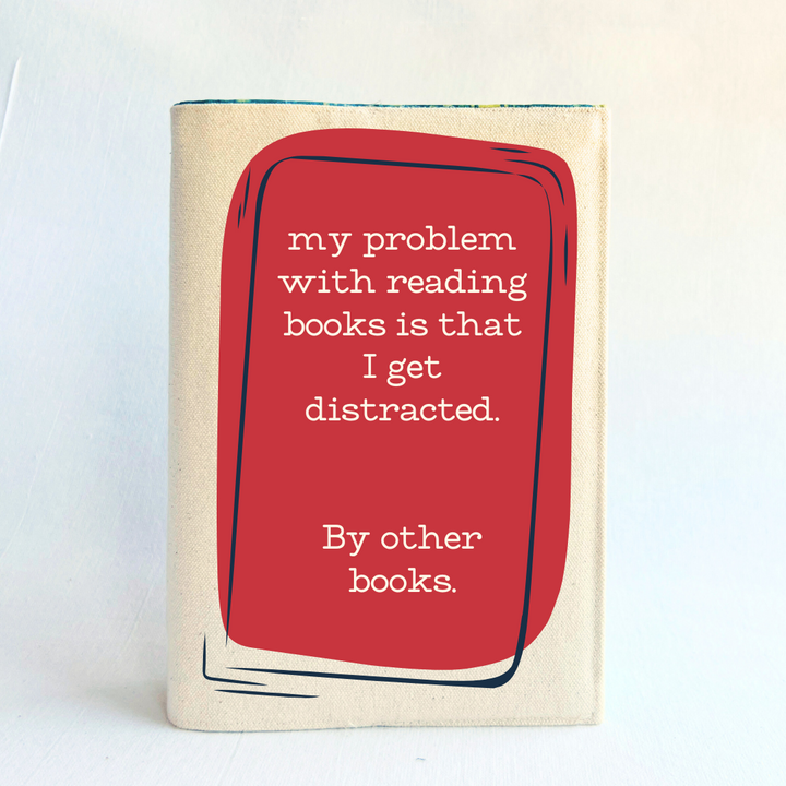 a book covered with a linen-colored canvas reusable book cover.  A rectangular design in cherry red tops the cover, with the words, 'my problem with reading is that I get distracted.  By other books.'