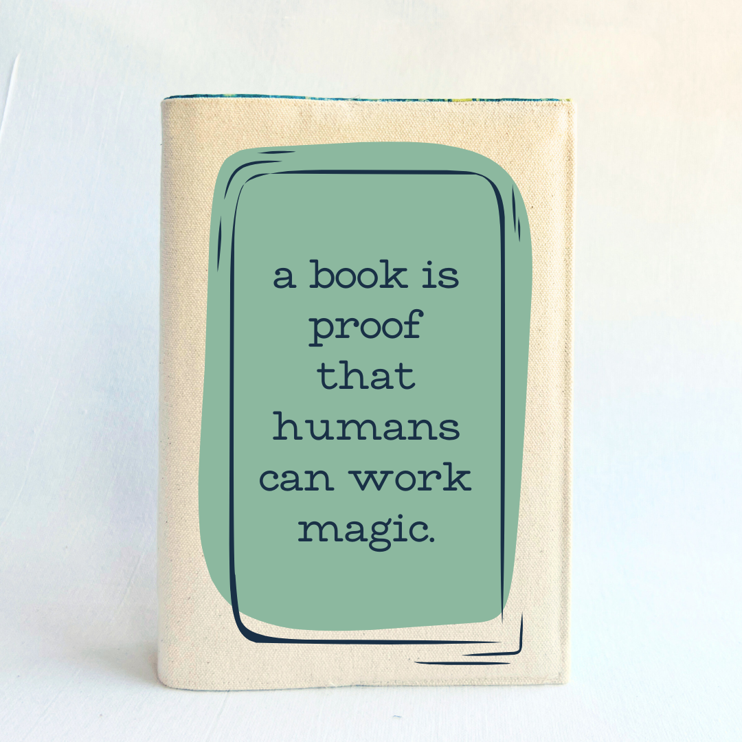a book covered with a linen-colored canvas reusable book cover. A rectangular design in sage green is featured in the center of the cover, with the words, 'a book is proof that humans can work magic.'