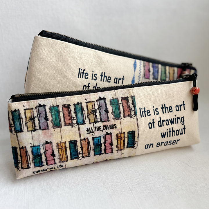 Rectangular zip bag in linen colored canvas and multicolored canvas. Black vinyl lettering decorates one side, with the words, "life is the art of drawing without an eraser." Used for pencil or art tools.